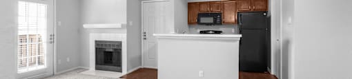 A spacious living room with a fireplace and a kitchenette in the background.