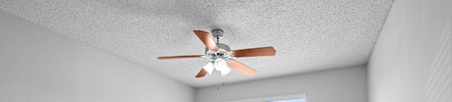 A room with a ceiling fan and a window overlooking a fence.