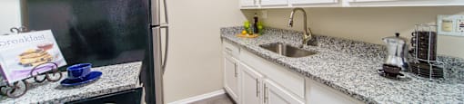 Grey hardwood like flooring with white cabinets, stainless steal appliances, and grey and white stone counter tops.