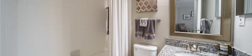 Bathroom with tub/shower combo, white cabinets, modern grey and white counters.