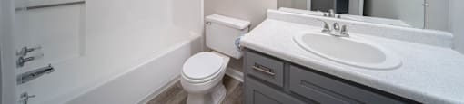 modern bathroom with tub, sink, toilet, mirror, and light