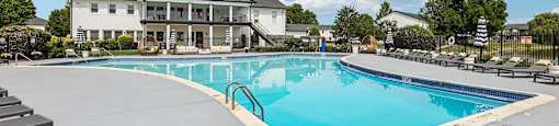 A large swimming pool in front of a white house.