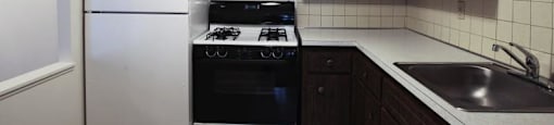 Dark kitchen cabinetry with beige tile flooring, beige tile backsplash, and white appliances with black accents.