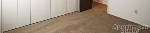 Bedroom with beige carpeting and white closet doors lining the entire right wall.