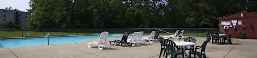 Outdoor pool with sundeck, lawn chairs surrounded by trees