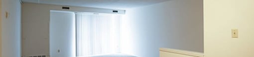 Living room with beige carpeting, vertical blinds on doorwall, and ceiling fan