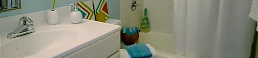Bathroom with white cabinetry and countertop.  Silver hardware, and mirror above sink.  Blue tile with green painted walls.  White tub surround with white tub, curved shower rod and white shower curtain.  Towels folded and on toilet.