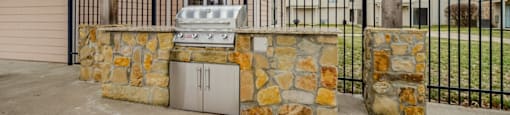 A patio with a grill and a stone wall.