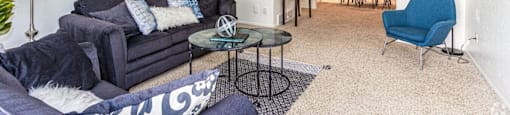A living room with a grey couch, a blue chair, and a glass table.