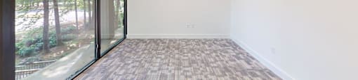 A room with a carpeted floor and a window overlooking a wooded area.