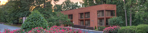 A building with the word "AVILK" on it is surrounded by greenery and flowers.