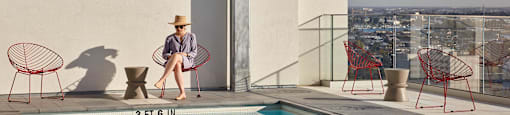 A woman in a hat sits on a chair by a pool.