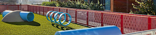 A playground with a red fence and blue and grey slides.