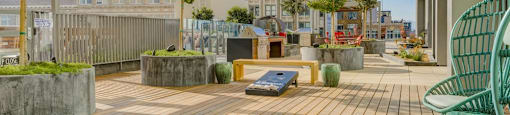 A wooden deck with a green chair and a bench in the foreground with a building in the background.