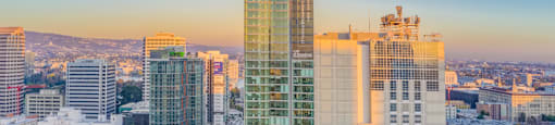 A cityscape with a mix of modern and older buildings, with the sun setting in the background.