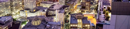 A cityscape at dusk with buildings illuminated against a twilight sky.