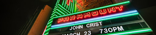 A brightly lit marquee sign for a show by John Crist on March 23 at 7:30 PM.