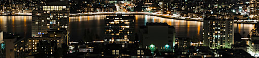 A cityscape at night with lights from buildings and a body of water.