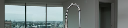 A modern kitchen with a stainless steel sink and a large window overlooking a cityscape.