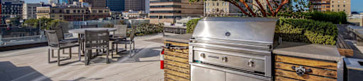 A stainless steel grill is on a patio with a city skyline in the background.