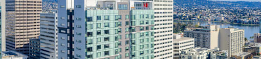 A tall building with a red logo on the side is surrounded by other buildings.