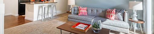 Living room with light blue walls, a couch, and coffee table next to kitchen with counter stools at Mullan Reserve Apartments in Missoula, MT