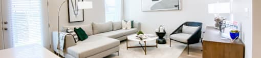 A modern living room with a white couch, a black chair, and a wooden cabinet.