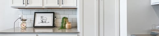 A kitchen with white cabinets and a framed picture on the counter.