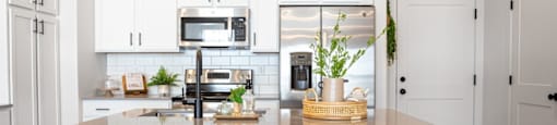 A kitchen with white cabinets and a white island with bar stools.