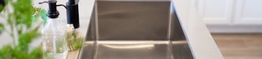 A kitchen sink with a black faucet and a bottle of soap on the counter.