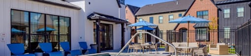 A pool area with a white building and blue chairs.