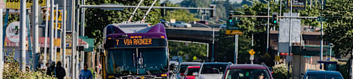 Bus at bus stop with Mount Rainier in the background and cars driving down the street.