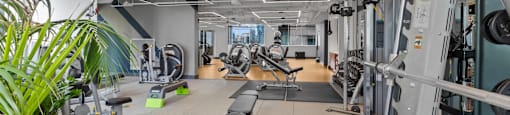 a gym with weights machines and other equipment in a building with a large window