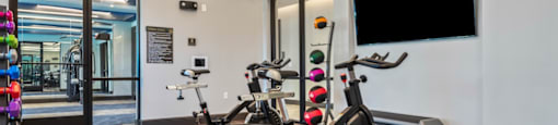 A gym with a row of stationary bikes and a flat screen TV mounted on the wall.