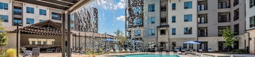 A swimming pool with a waterfall and a building in the background.