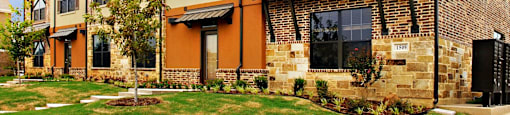 A brick building with a green lawn in front at Centre Place Apartments, Denton, TX