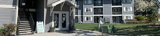 a gray apartment building with a lawn and trees in front of it