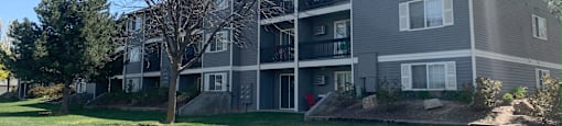 a gray apartment building with a green lawn and trees