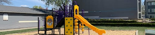 a playground with a slide and swings in front of a building