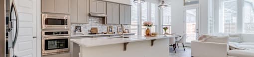 A modern kitchen with a refrigerator on the left and a dining area with a white couch.