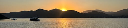 a sunset over a lake with boats and mountains in the background
