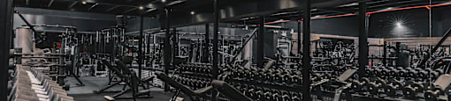 A gym with a variety of equipment including dumbbells, weight plates, and benches.