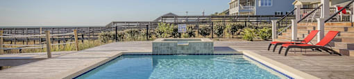 A swimming pool with a wooden deck and a red bench.