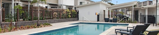 A pool surrounded by lounge chairs and a fence.