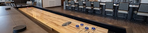 a shuffleboard table in the center of a large room with chairs and a television