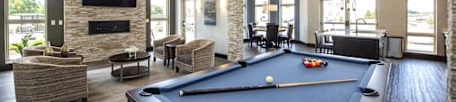 A pool table is in the middle of a room with a stone fireplace and a television above it.