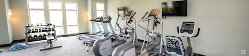 a gym with cardio machines and a tv
