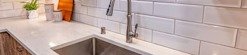 a kitchen sink with white subway tiles and wooden cabinets