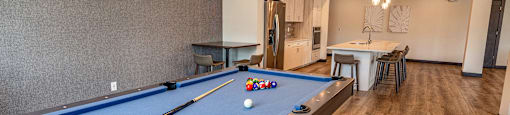 a pool table in a clubhouse with a bar and a kitchen
