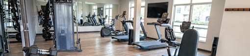 a gym with cardio machines and weights on a wooden floor